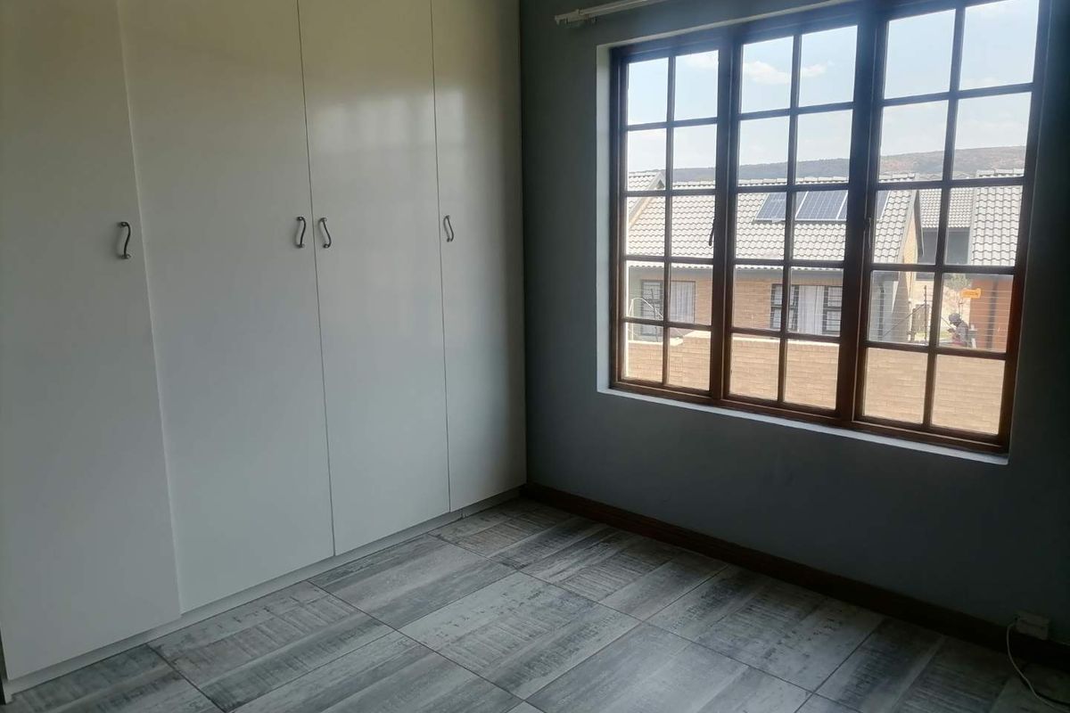 A bright bedroom featuring built-in white cabinetry, large paneled windows, and modern grey wood-look floor tiles.