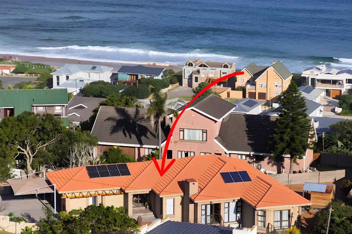 Aerial view of a coastal residential property featuring a tiled roof with integrated solar panels, situated in a prime seaside location.