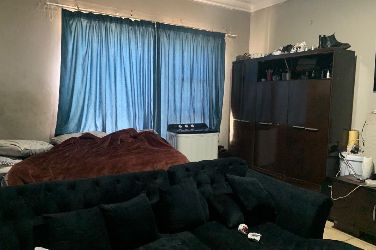 A bedroom space featuring tiled flooring, crown molding, and large window coverage, currently utilized as a multi-purpose living and sleeping area.