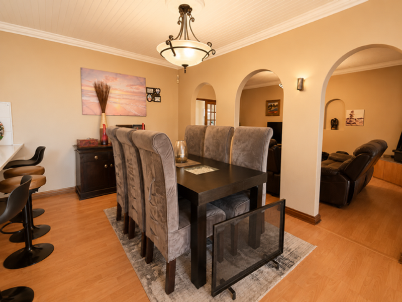 Dining room featuring laminate flooring, decorative archways leading to the living area, and a beadboard ceiling with crown molding.