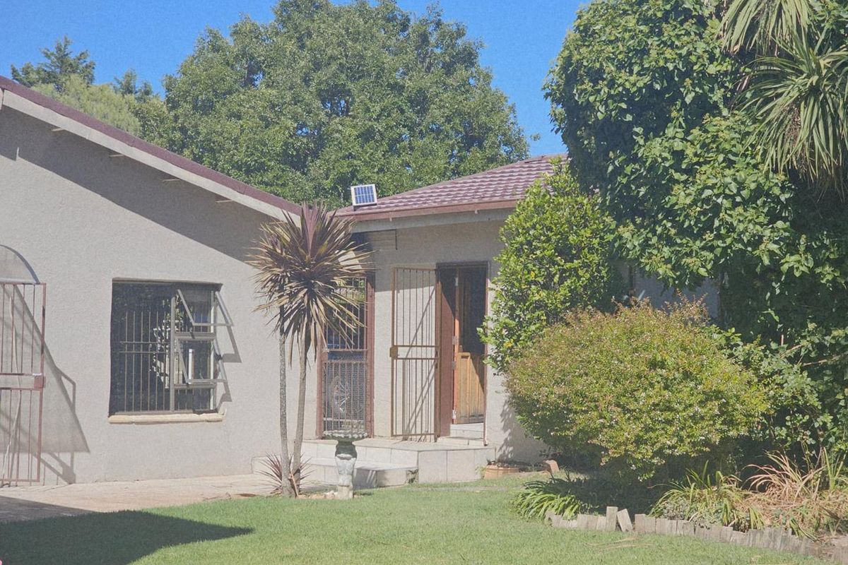 A view of the rear exterior of the house featuring a paved patio area, established garden, and security gates on the entrance doors.