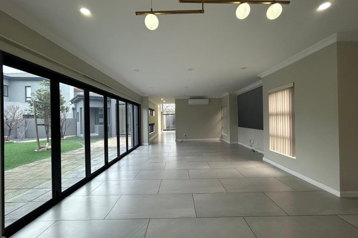 Spacious, open-plan living area featuring large format floor tiles, modern lighting, and expansive stacking glass doors providing seamless access to the garden.