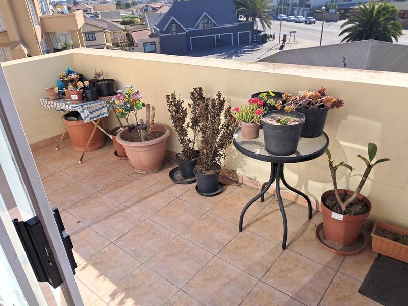 An open-air balcony featuring tiled flooring and a low parapet wall, offering an elevated view of the surrounding neighborhood.
