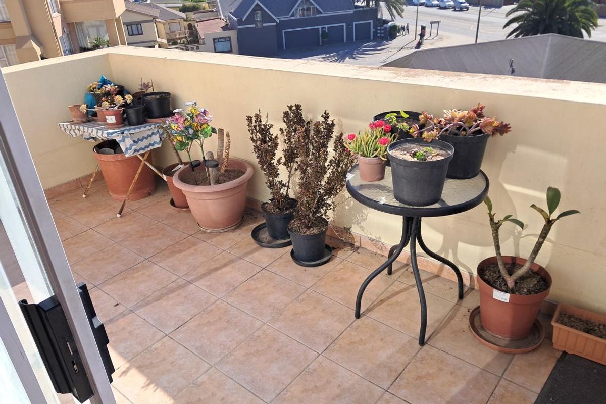 An open-air balcony featuring tiled flooring and a low parapet wall, offering an elevated view of the surrounding neighborhood.
