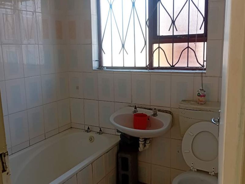 A dated bathroom featuring a bathtub, pedestal basin, and toilet, with tiled walls and floors, requiring renovation to update the finishes and fixtures.