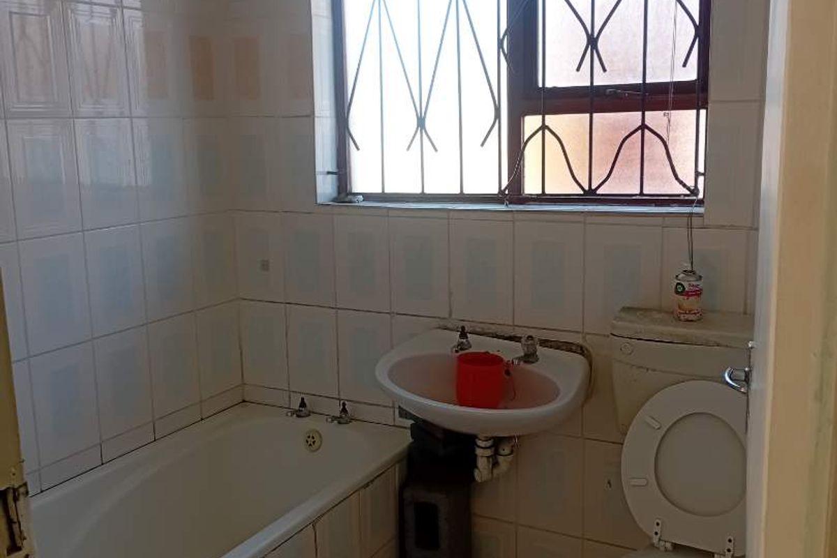 A dated bathroom featuring a bathtub, pedestal basin, and toilet, with tiled walls and floors, requiring renovation to update the finishes and fixtures.