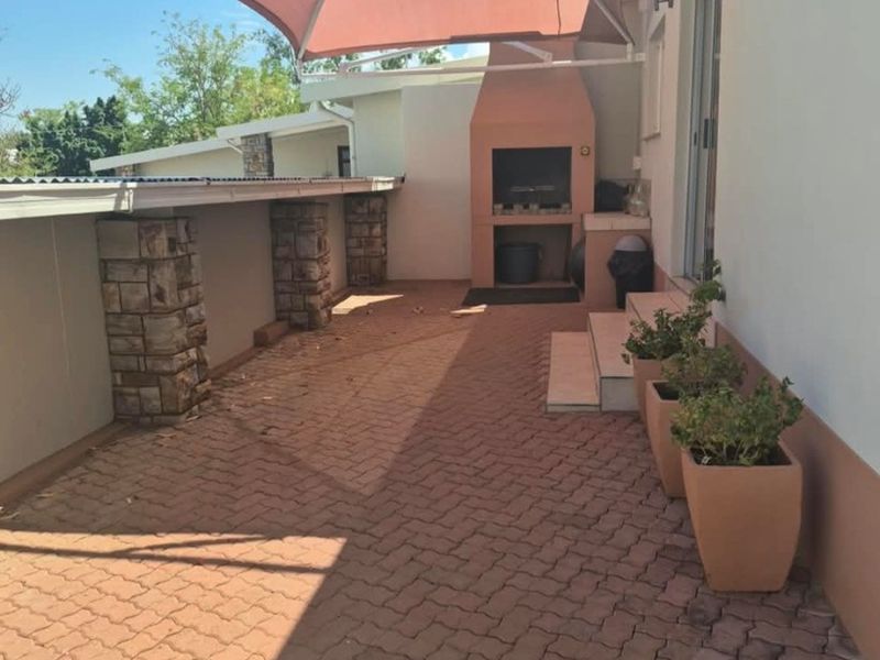 Outdoor patio area featuring a built-in braai, stone-clad pillars, and a shade sail, providing a functional space for outdoor entertaining.