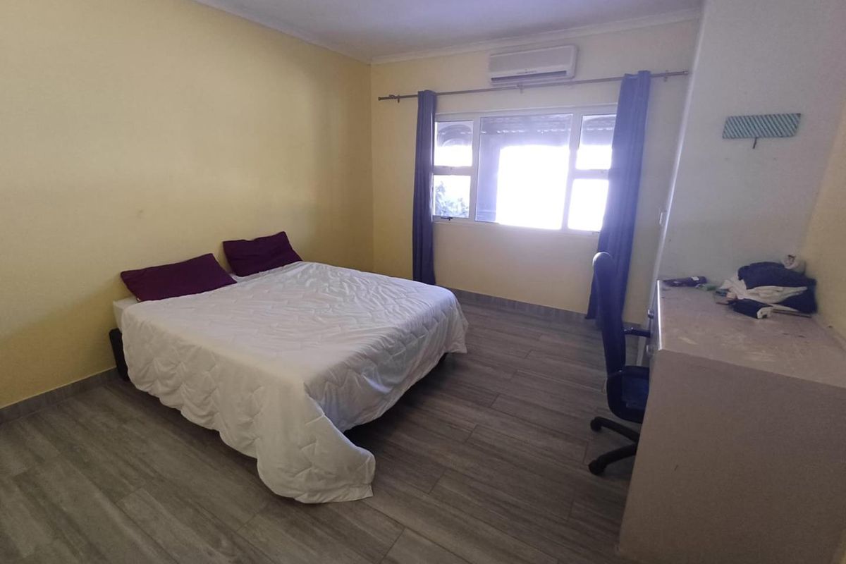 A bedroom featuring wood-look tile flooring, a wall-mounted air conditioning unit, and a large window with curtain rod.