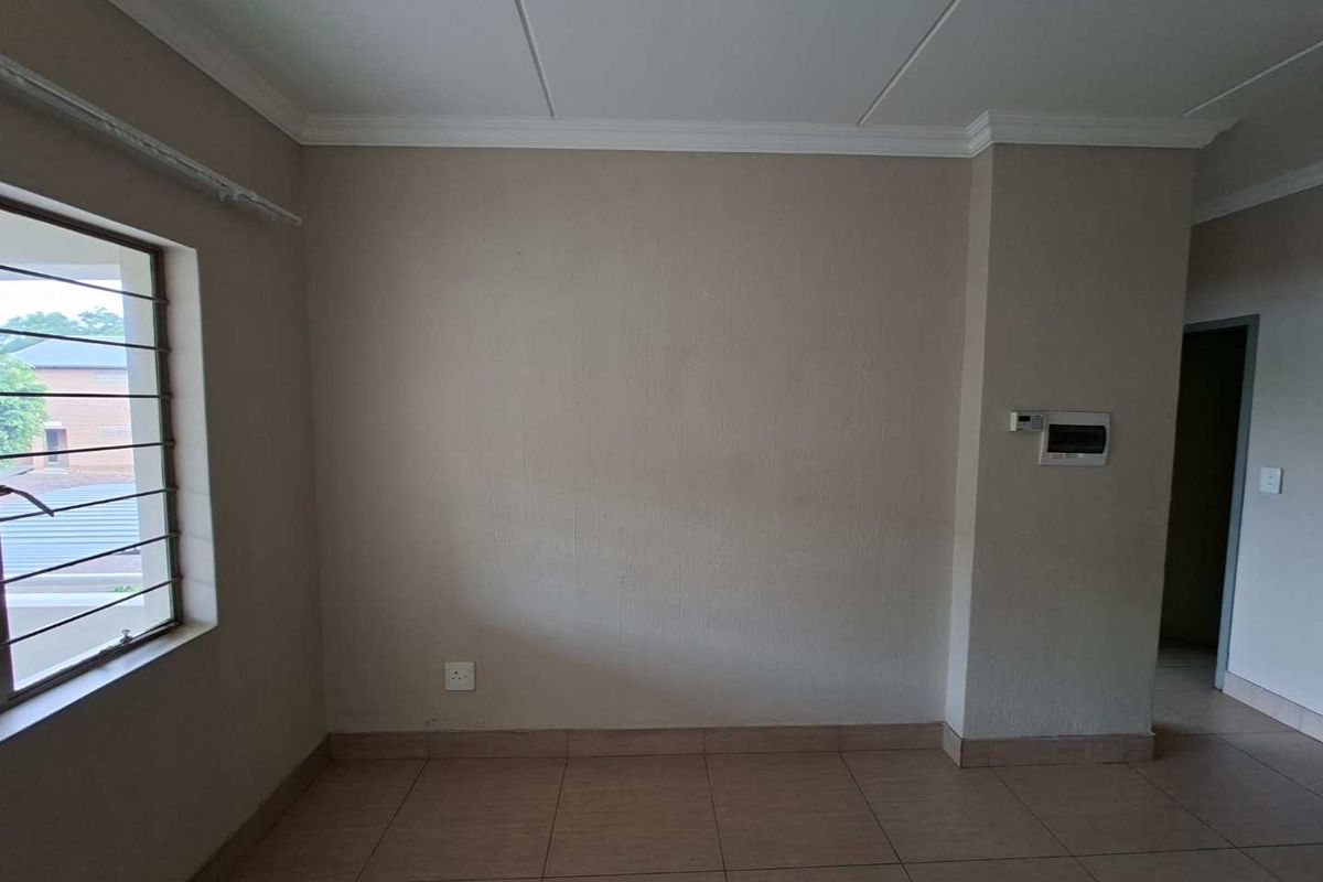 A neutral, empty room featuring tiled flooring, crown molding, and a security-barred window, providing a versatile space ready for personalization.