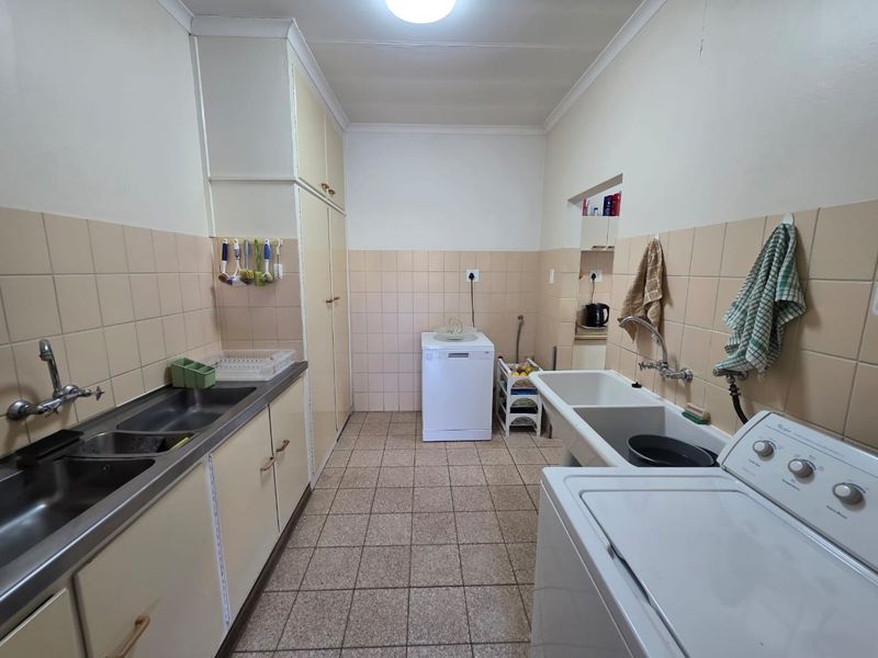 Functional laundry room featuring built-in cabinetry, double stainless steel sink, utility basin, and tiled splashbacks with ceramic floor tiles.