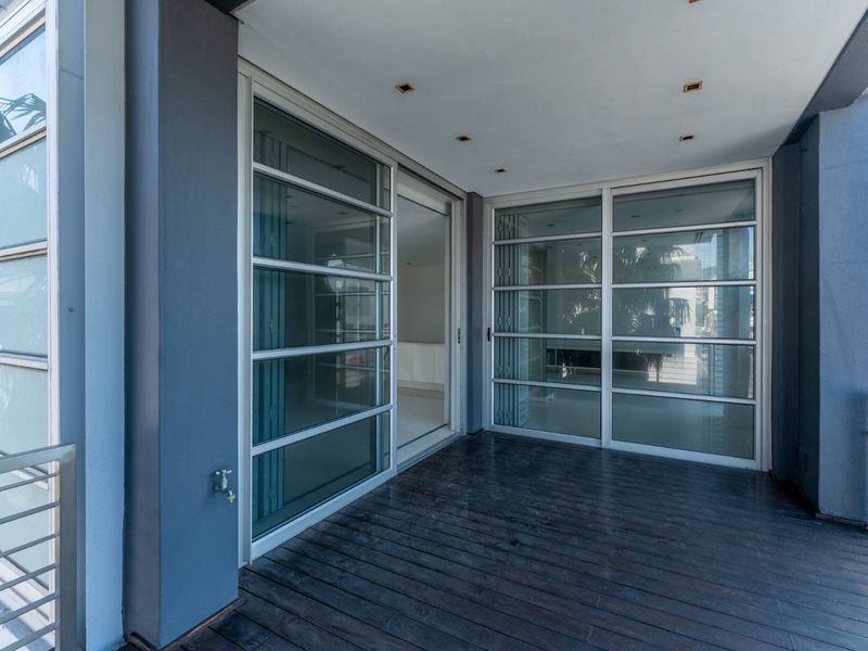 A spacious covered balcony featuring timber decking, stainless steel balustrades, and large sliding glass doors providing access to the interior living area.