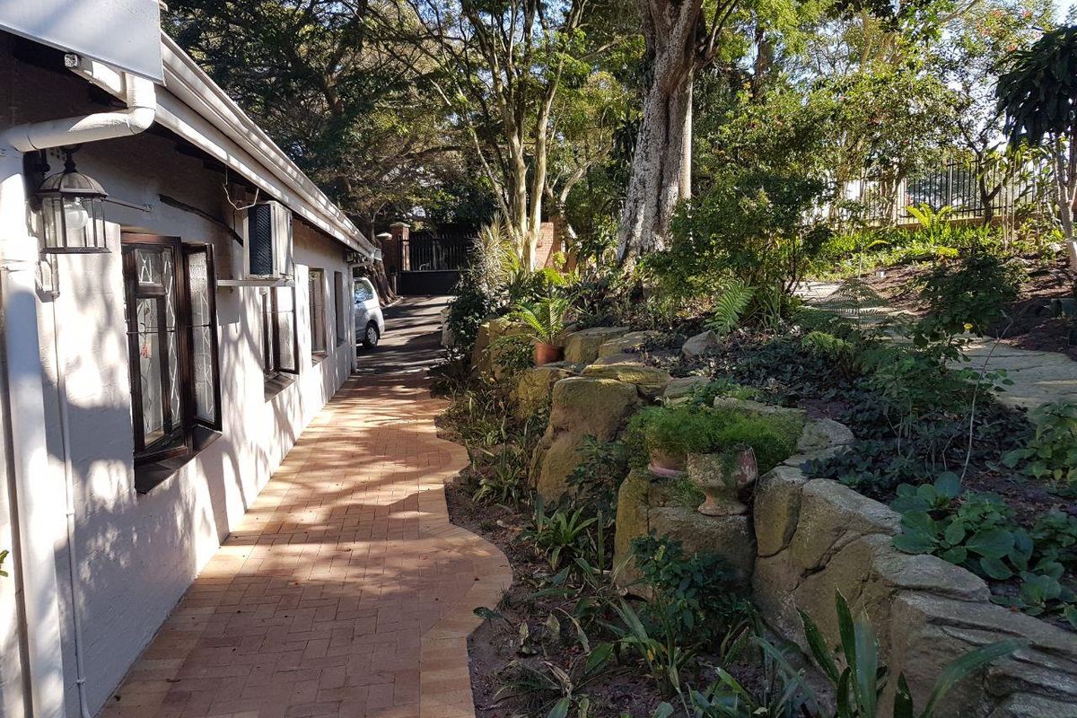 A paved side walkway along the exterior of the house, featuring a natural stone retaining wall and established garden landscaping.