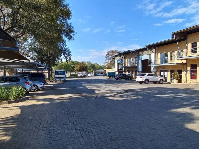 Exterior view of an industrial complex featuring paved parking, shade cloth carports, and multi-level brick units with roller shutter doors and balconies.