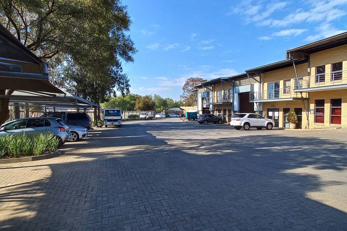 Exterior view of an industrial complex featuring paved parking, shade cloth carports, and multi-level brick units with roller shutter doors and balconies.