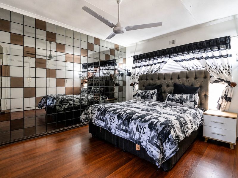 Spacious bedroom featuring a large mirrored feature wall, ceiling fan, and warm-toned laminate flooring.