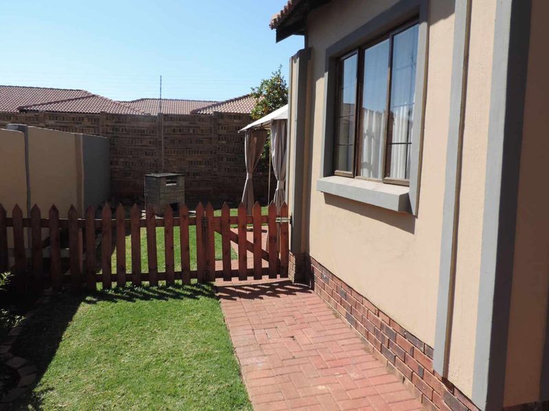 A private rear garden area featuring brick paving, a wooden picket fence, and a built-in braai, enclosed by a brick boundary wall.