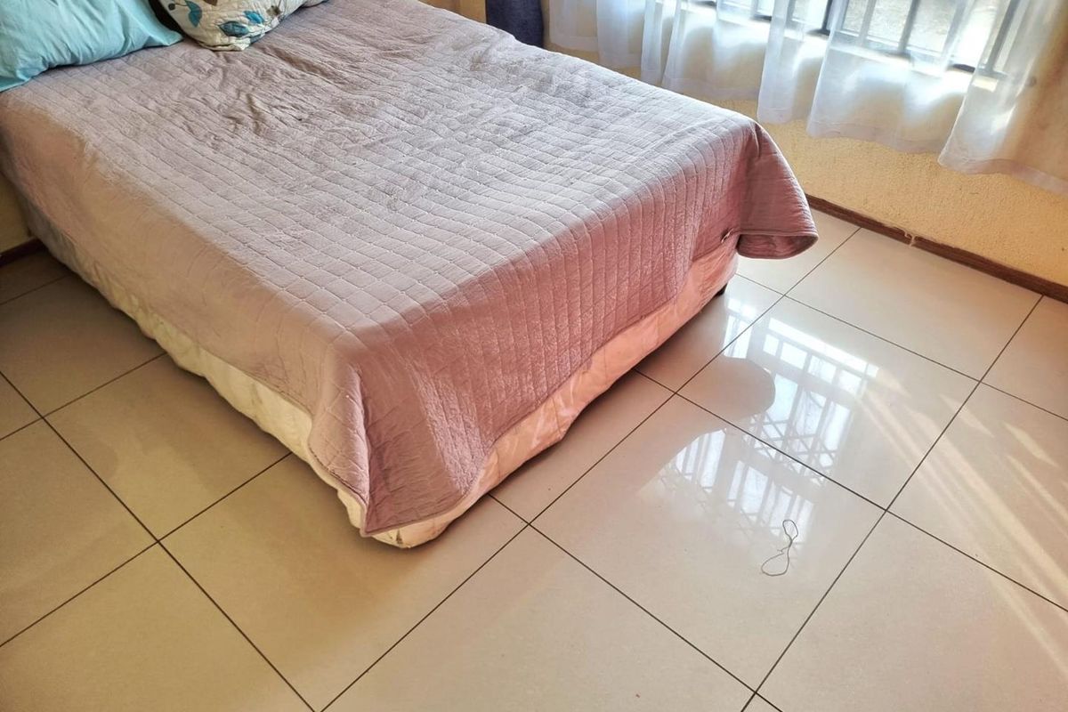 A bedroom featuring light-colored tiled flooring and a window fitted with security bars, providing natural light to the space.