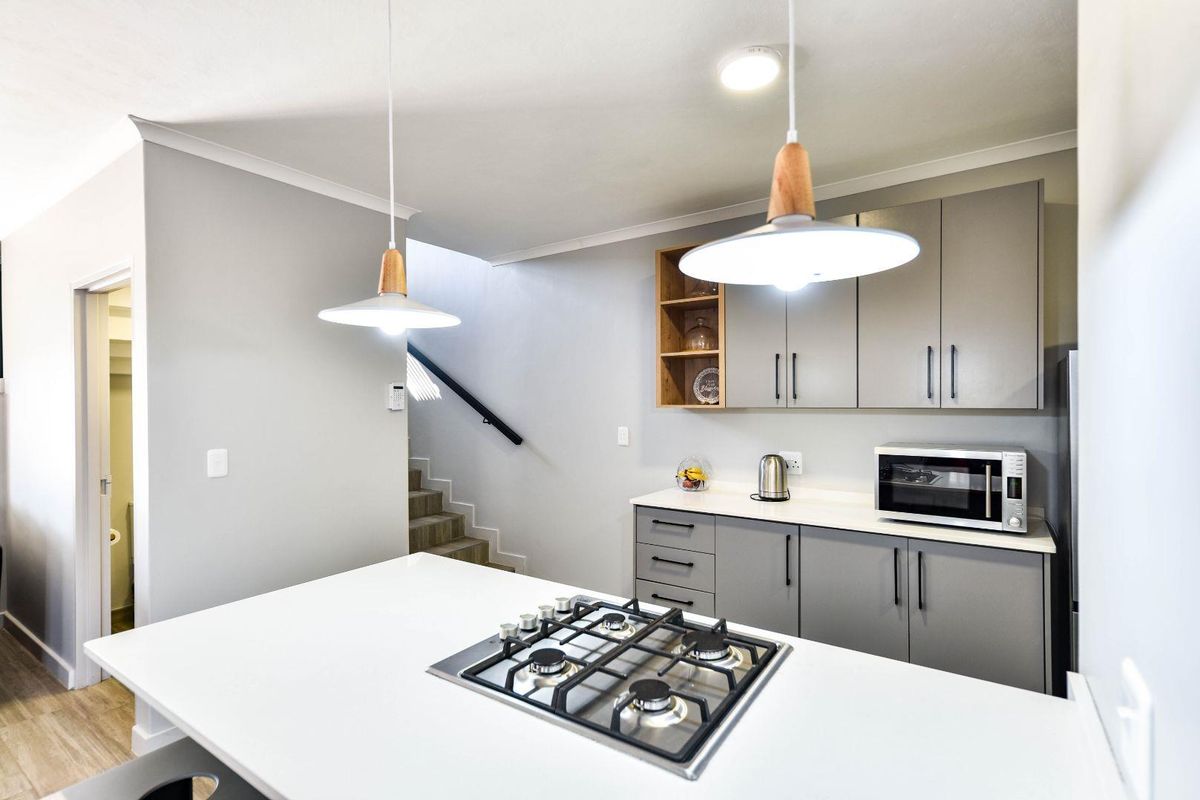 Modern kitchen featuring grey cabinetry, white quartz countertops, a built-in gas hob, and pendant lighting, with an adjacent staircase.