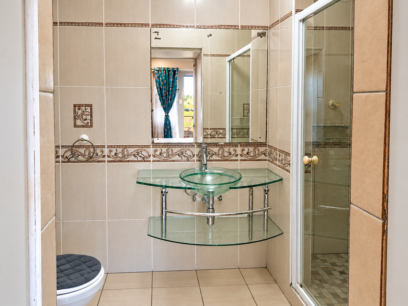 A functional bathroom featuring a glass vessel sink, chrome fixtures, tiled walls with decorative accents, and a separate shower enclosure.