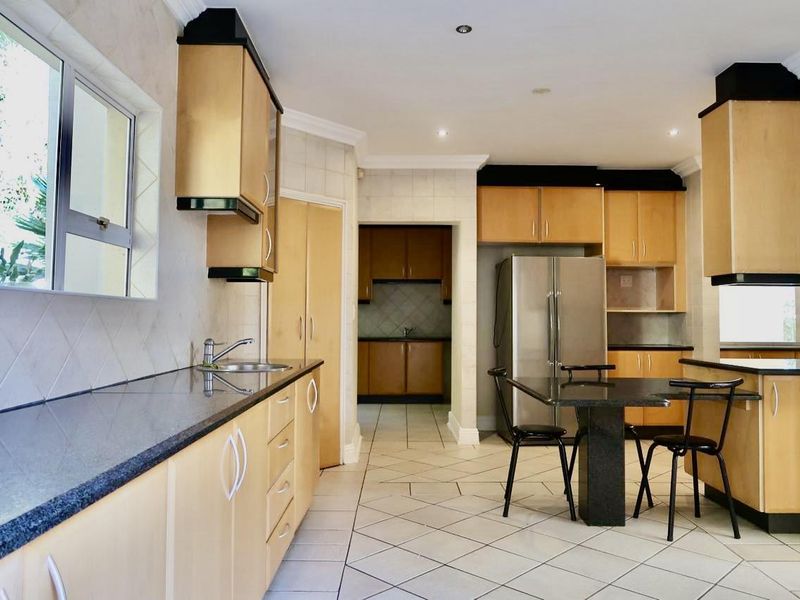 Spacious kitchen featuring light wood cabinetry, granite countertops, tiled flooring, and an adjoining scullery area with additional storage and prep space.