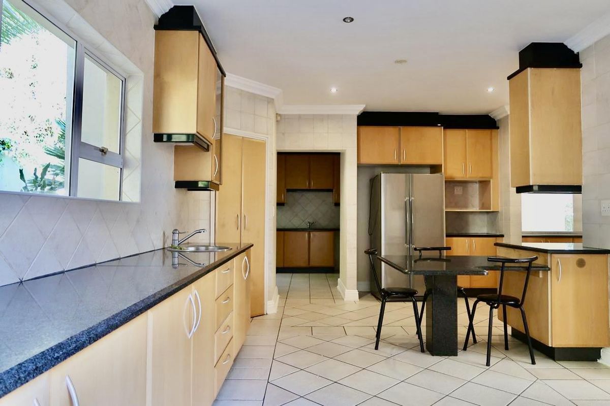 Spacious kitchen featuring light wood cabinetry, granite countertops, tiled flooring, and an adjoining scullery area with additional storage and prep space.