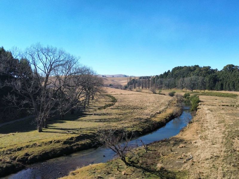 An expansive aerial view of the farm landscape featuring a natural river winding through open pastures and surrounding woodland.