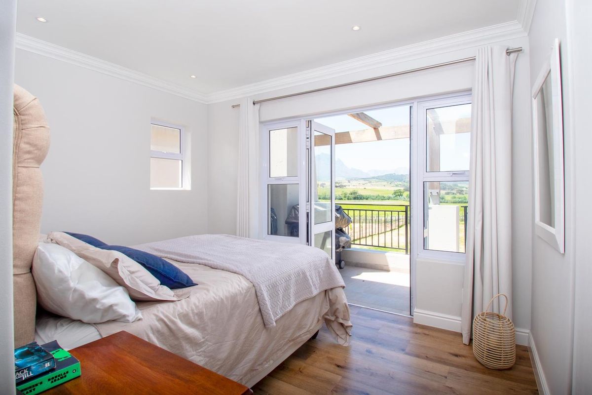Bright bedroom featuring wood-look flooring, recessed lighting, and double doors opening onto a private balcony with scenic mountain and landscape views.