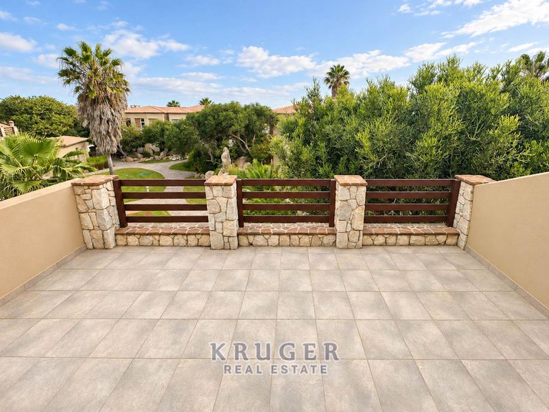 A spacious balcony featuring tiled flooring and a decorative stone and timber balustrade, overlooking the estate grounds.