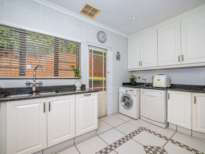 A functional laundry room featuring white built-in cabinetry, granite countertops, a stainless steel sink, and tiled flooring with decorative accents.