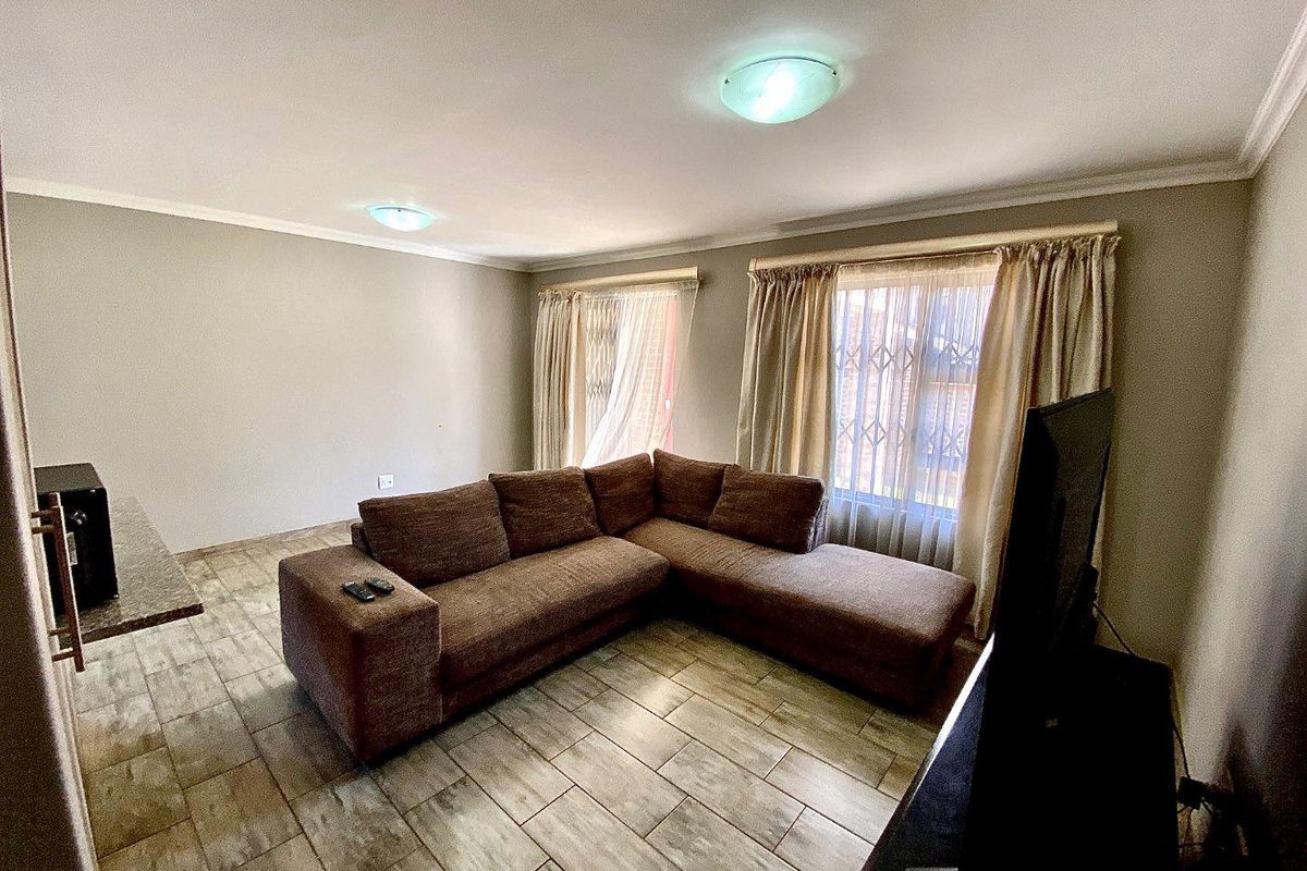A living room featuring tiled flooring, dual flush-mount ceiling lights, and security gates on the windows.