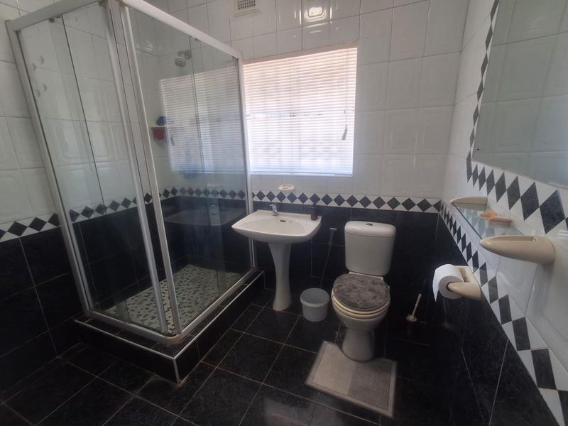 A functional bathroom featuring a glass shower enclosure, pedestal sink, toilet, and contrasting black and white tiled finishes.