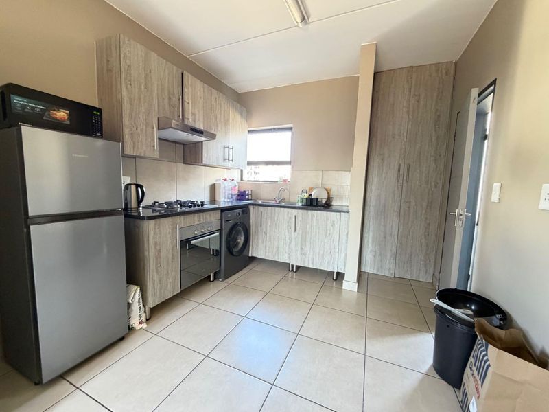 Functional kitchen featuring wood-look cabinetry, gas hob, electric oven, extractor fan, and tiled flooring with an integrated pantry cupboard.