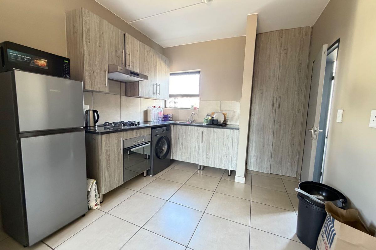 Functional kitchen featuring wood-look cabinetry, gas hob, electric oven, extractor fan, and tiled flooring with an integrated pantry cupboard.