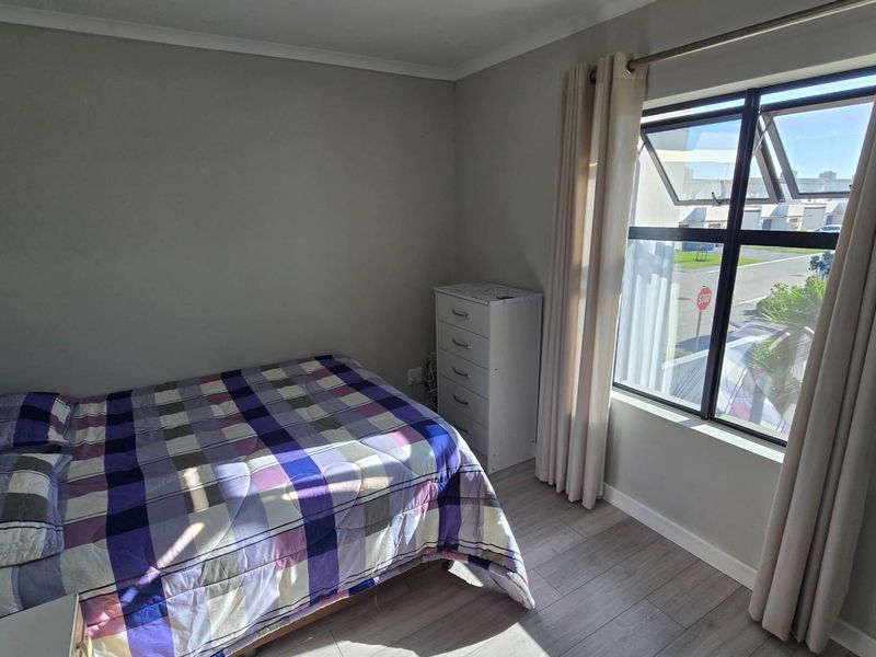 A functional bedroom featuring light-toned laminate flooring, neutral wall finishes, and a large window allowing for natural light.