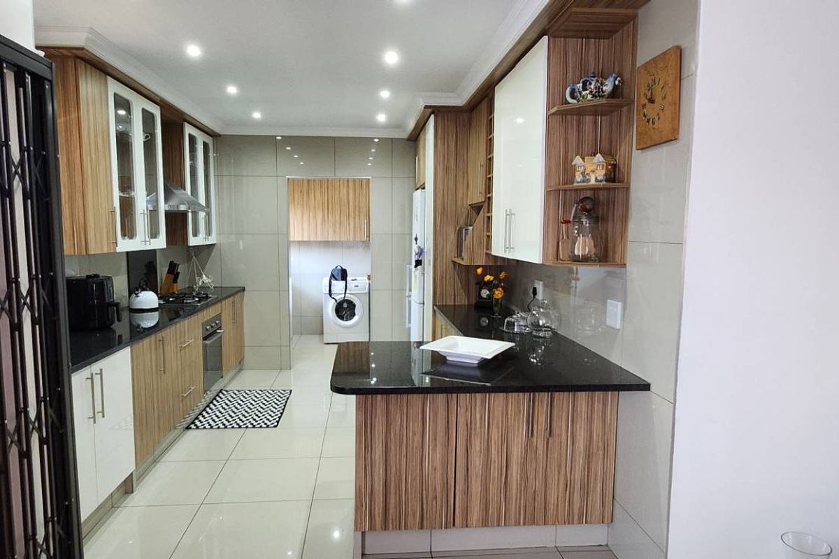 Modern kitchen featuring wood-grain cabinetry, black granite countertops, integrated hob and oven, and a seamless transition to a dedicated laundry area.