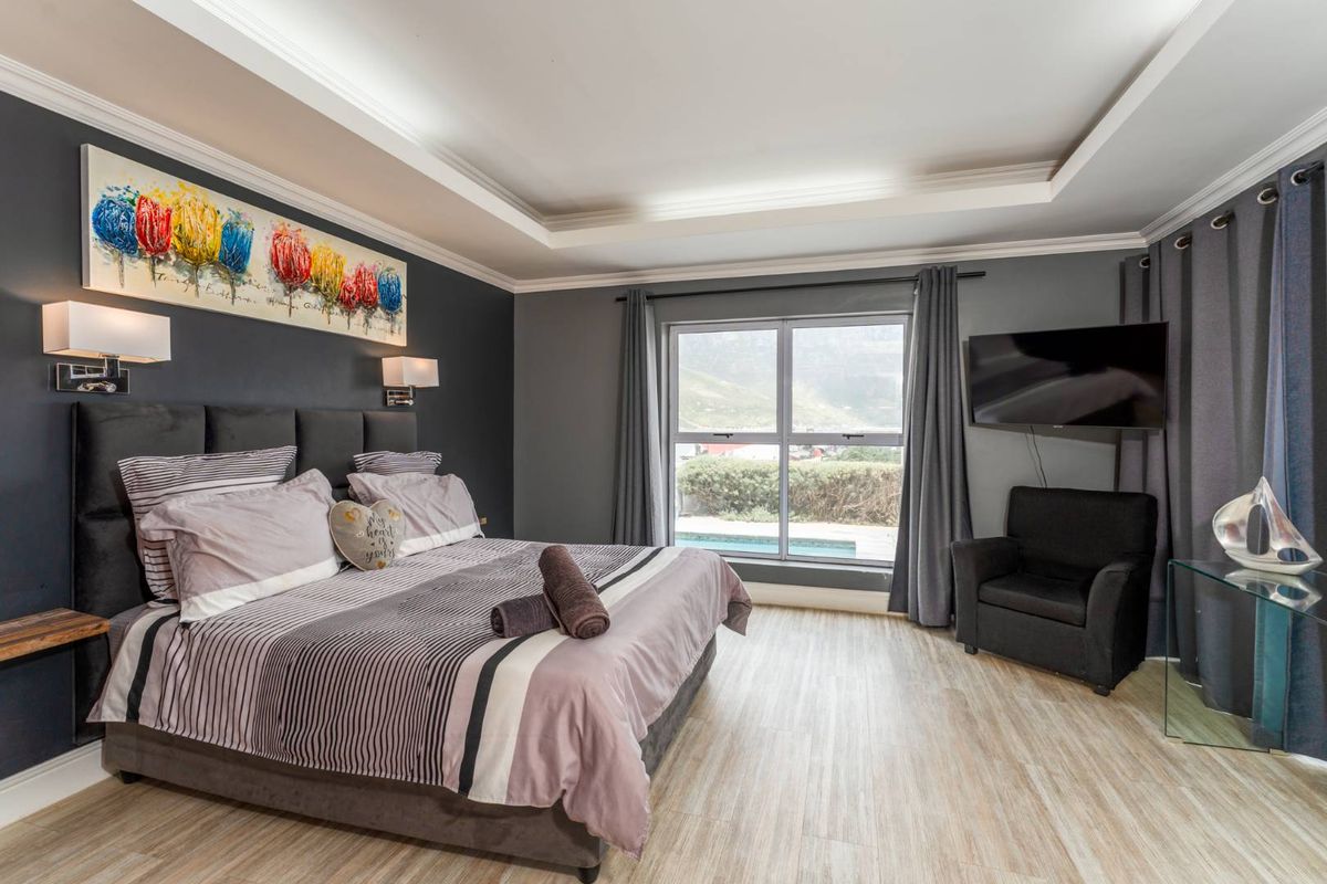 Spacious bedroom featuring a tray ceiling, modern wood-look flooring, and large windows with views of the outdoor pool area.