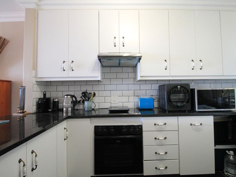 A well-maintained kitchen featuring white cabinetry, black granite countertops, a subway tile backsplash, and integrated appliances including an oven and extractor fan.