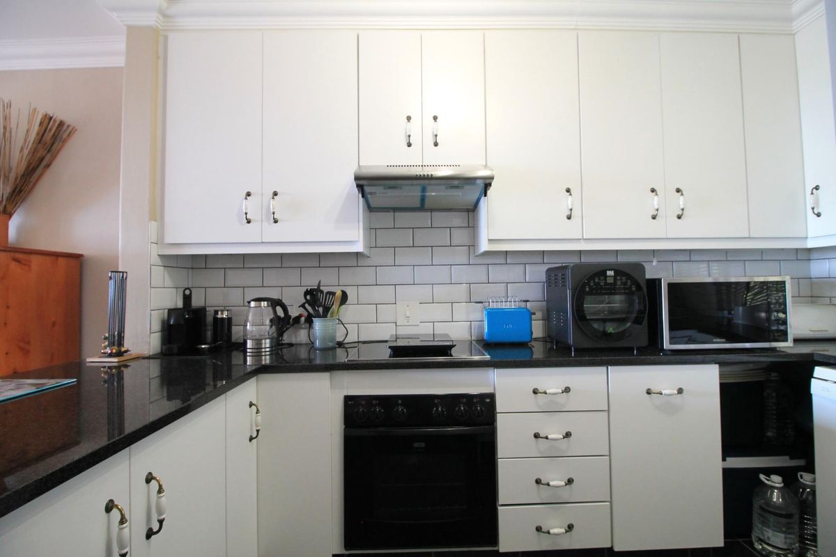A well-maintained kitchen featuring white cabinetry, black granite countertops, a subway tile backsplash, and integrated appliances including an oven and extractor fan.