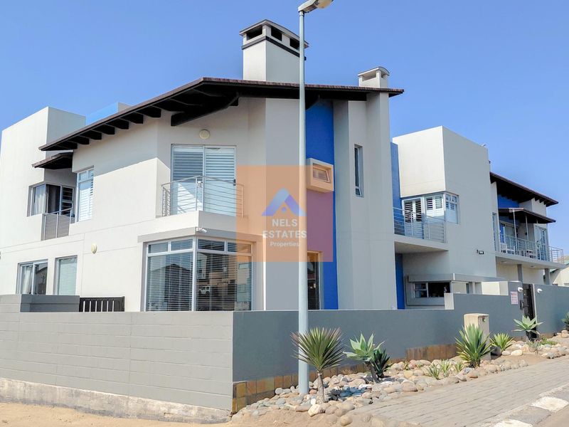 Modern multi-story residential property featuring a contemporary facade, balconies, and a secure boundary wall with paved street-side landscaping.