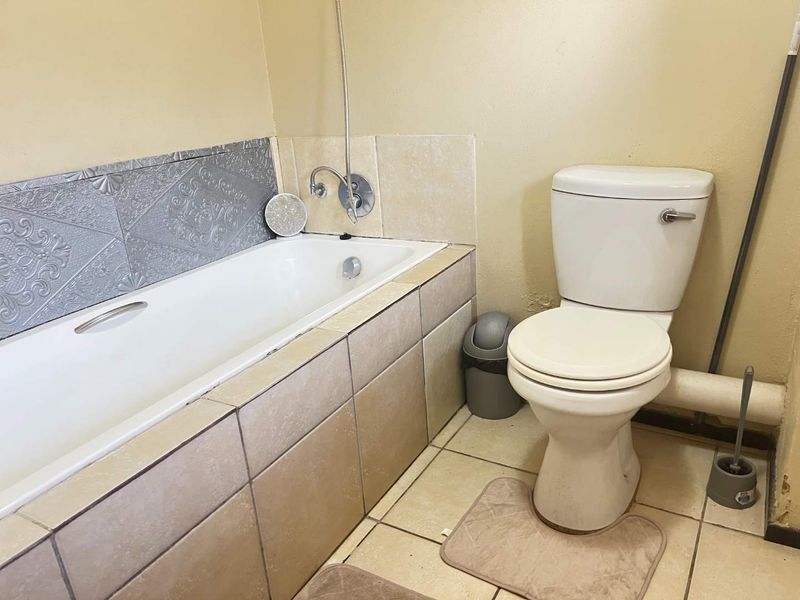 A functional bathroom featuring a bathtub with tiled surround and a standard toilet, requiring cosmetic updates to the wall finishes and grout.