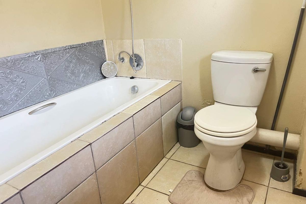 A functional bathroom featuring a bathtub with tiled surround and a standard toilet, requiring cosmetic updates to the wall finishes and grout.