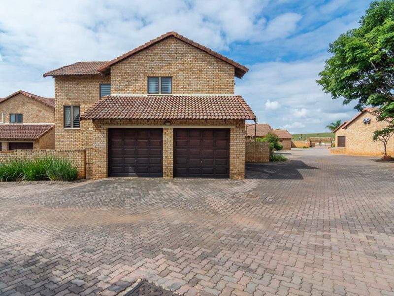 Front view of a townhouse featuring a double garage, face-brick exterior, and a paved driveway within a residential complex.