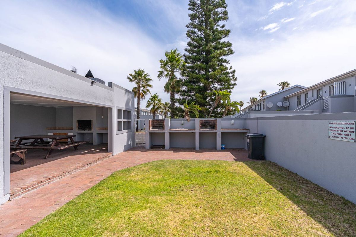 Communal outdoor entertainment area featuring a covered patio with built-in braai facilities, brick paving, and a landscaped lawn.