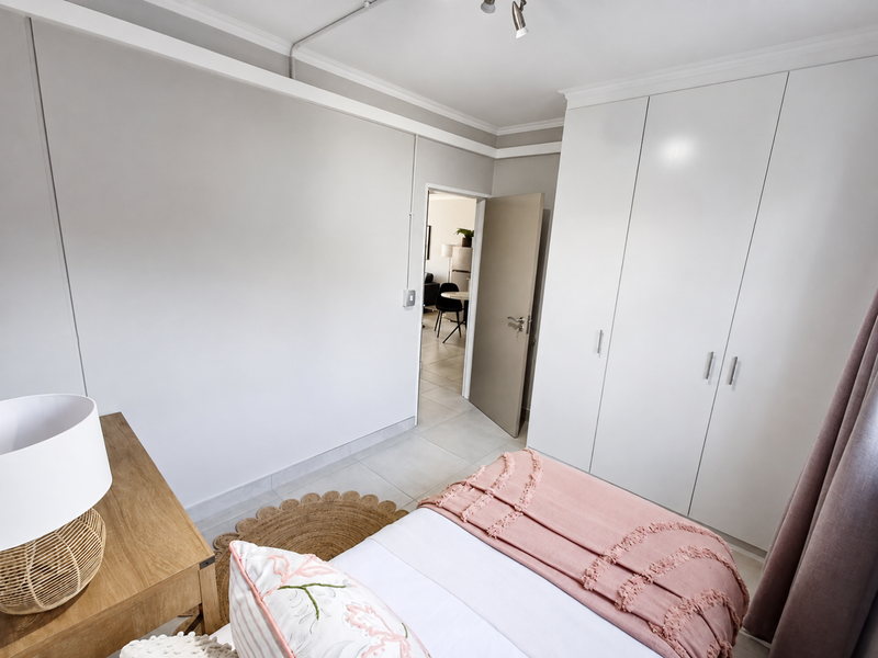 A well-maintained bedroom featuring neutral walls, tiled flooring, and ample built-in cupboard storage with clean finishes.