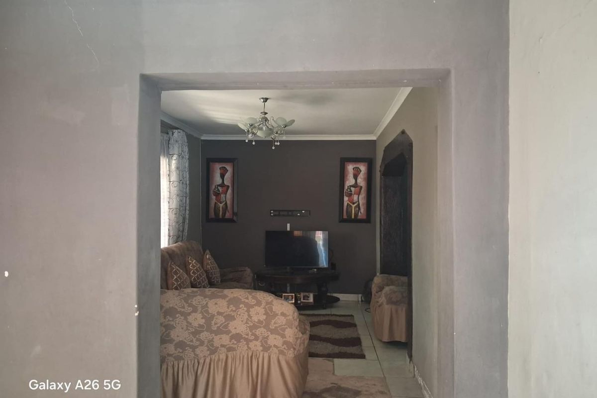 A living room area featuring tiled flooring and a central light fixture, currently showing unfinished wall surfaces and plastering work.
