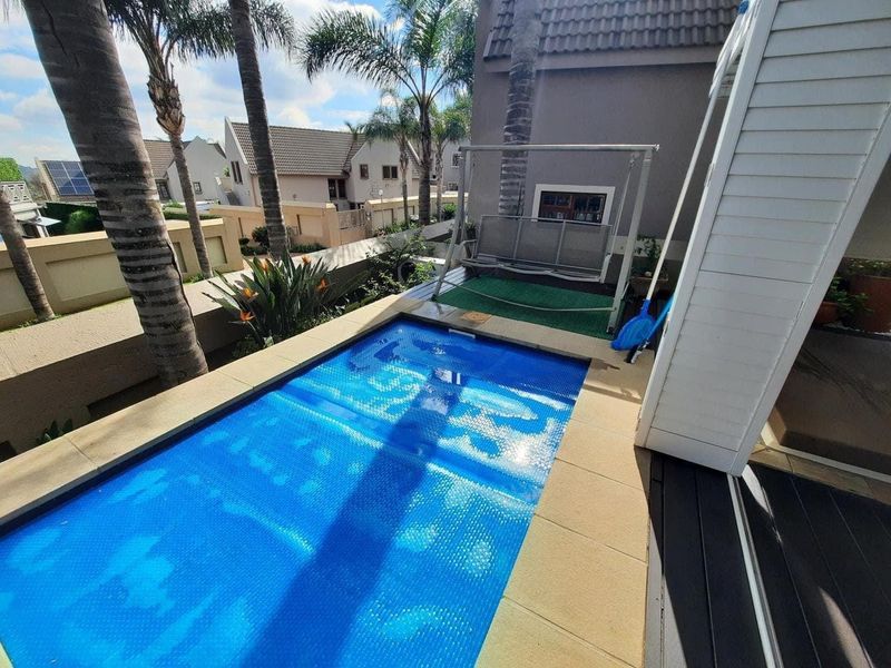 A compact swimming pool area featuring a blue pool cover, paved surround, and adjacent decking in a townhouse setting.