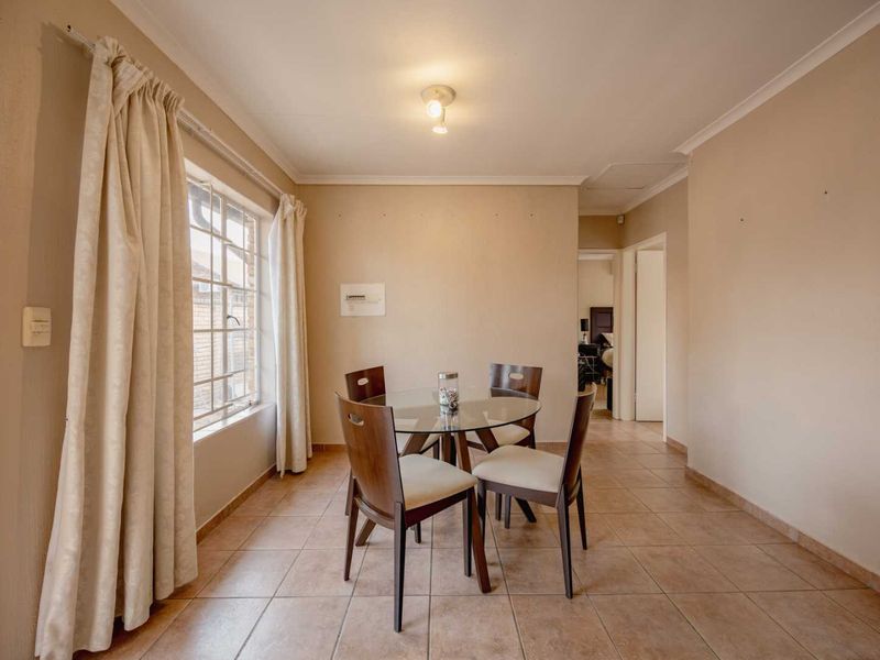 A functional dining area featuring tiled flooring, neutral wall tones, and a window with security bars, providing a bright and practical space.