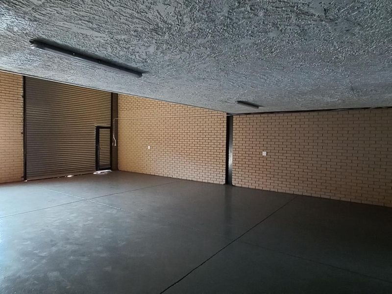 Spacious industrial warehouse area featuring exposed brick walls, polished concrete flooring, and a large roller shutter door for easy access.