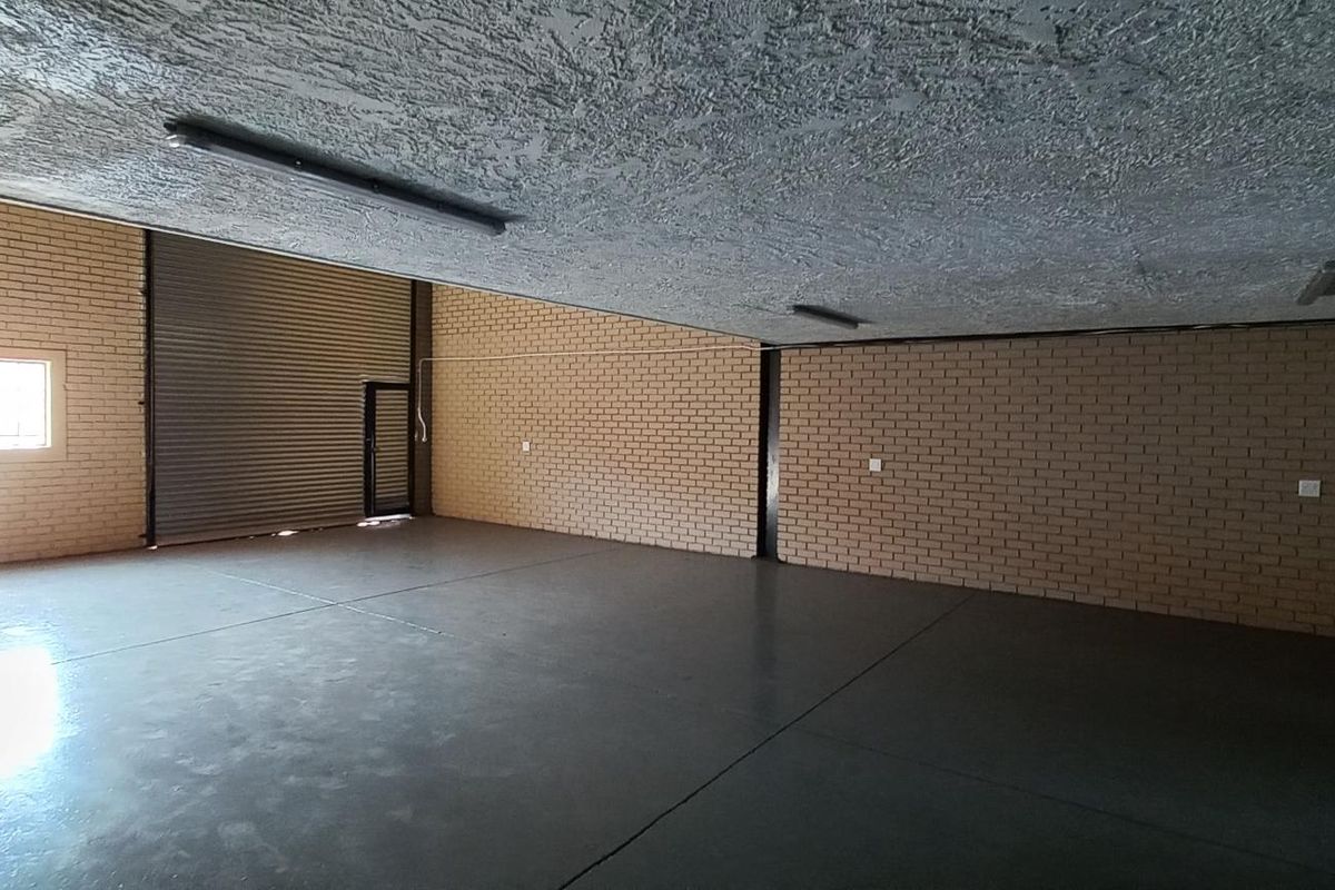 Spacious industrial warehouse area featuring exposed brick walls, polished concrete flooring, and a large roller shutter door for easy access.