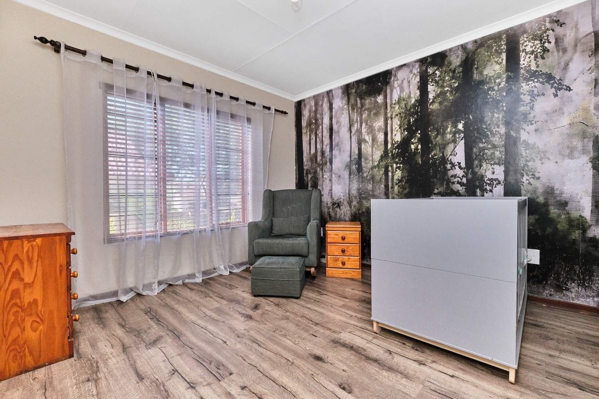 A bedroom featuring wood-look laminate flooring, a large window with venetian blinds, and a decorative forest-themed feature wall.